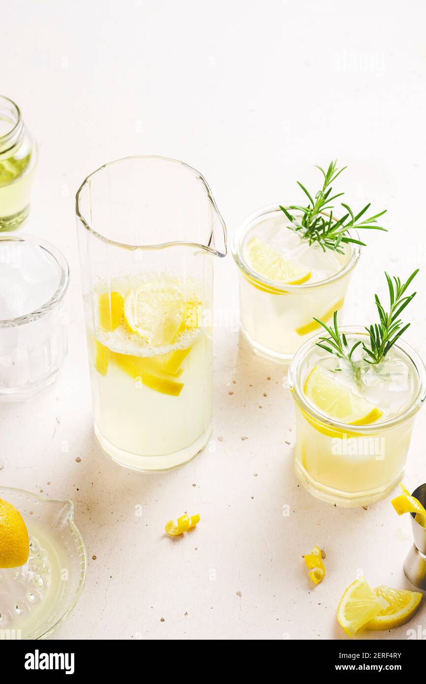 2 bicchieri e una brocca di limonata guarnita con scorza di limone e fette e rametti di rosmarino, posti su uno sfondo bianco con spazio per il testo. Foto Stock