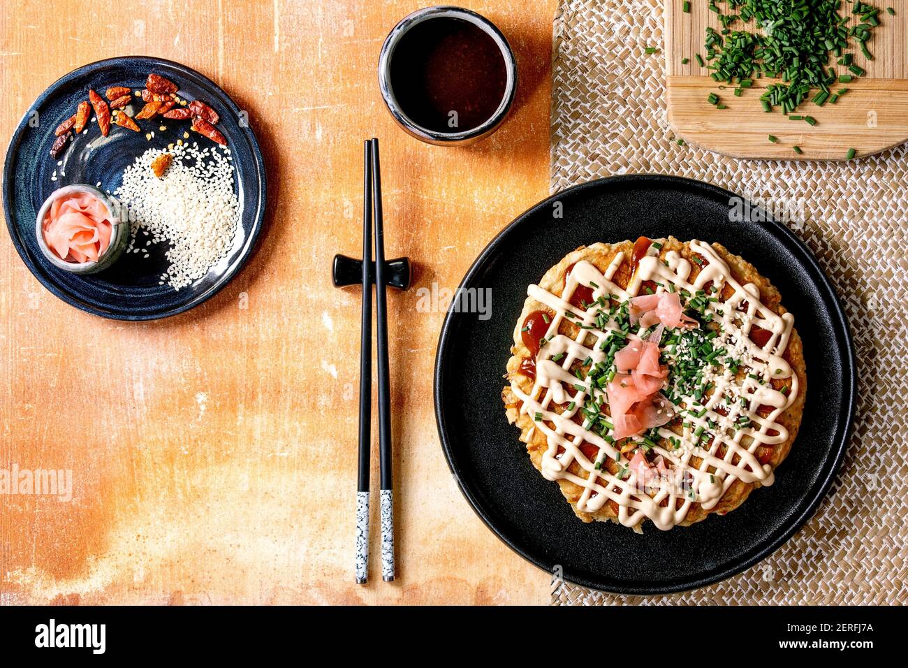 Frittella di cavolo okonomiyaki giapponese fatta in casa decorata con cipollina, zenzero sottaceto, salsa mayo su piastra di ceramica nera con chopsticks A. Foto Stock