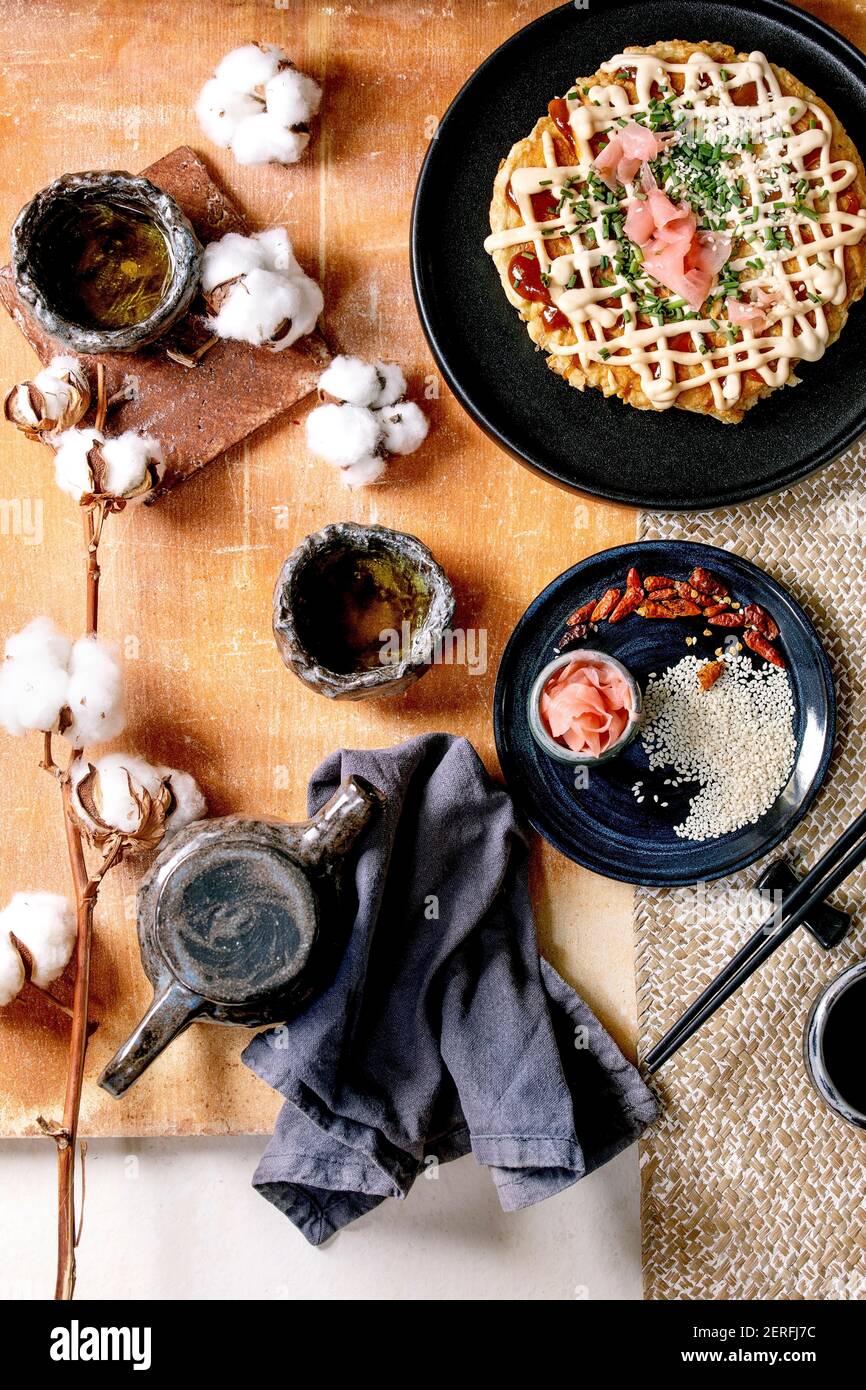 Frittella di cavolo okonomiyaki giapponese fatta in casa con cipolla, zenzero sottaceto, salsa mayo su piastra di ceramica nera. Bastoncini di pollo, teiera, cotone, Ing Foto Stock