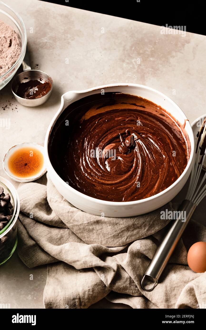 Ciotola di pastella brownie seduta su un tavolo accanto a gocce di cioccolato e farina. Foto Stock