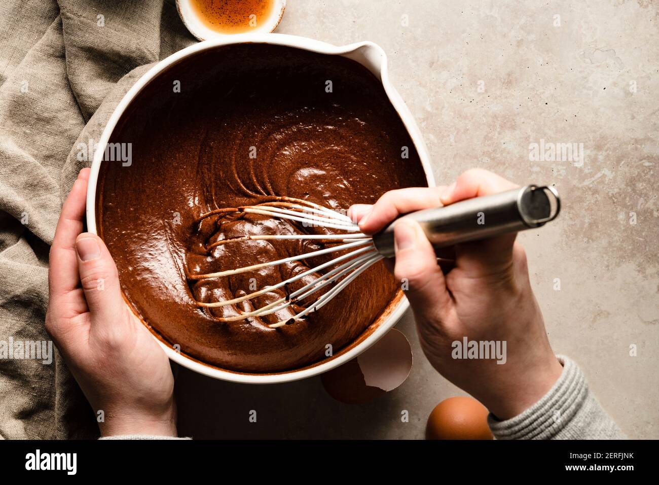 Mani che mescolano una ciotola di pastella di brownie vicino a ciotole di farina e scaglie di cioccolato. Foto Stock