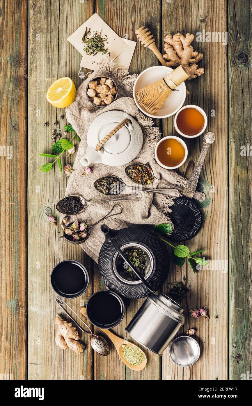 Vari tè e teiera composizione, erbe essiccate, tè verde, nero e tè matcha su fondo tavola di legno, piatto Foto Stock
