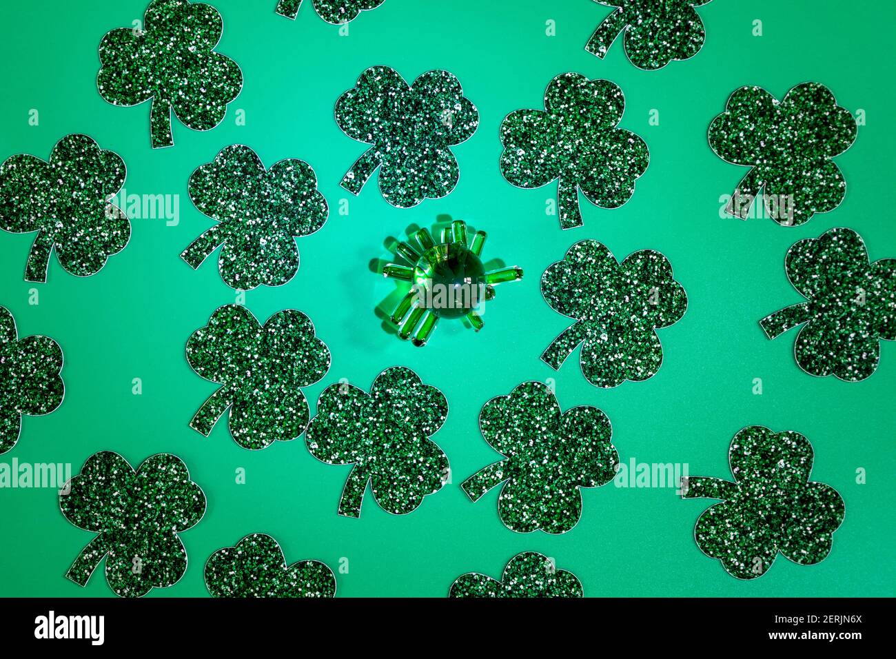 Composizione piatta con foglie di trifoglio e una figurina di vetro verde su sfondo verde. Giorno di San Patrizio Foto Stock