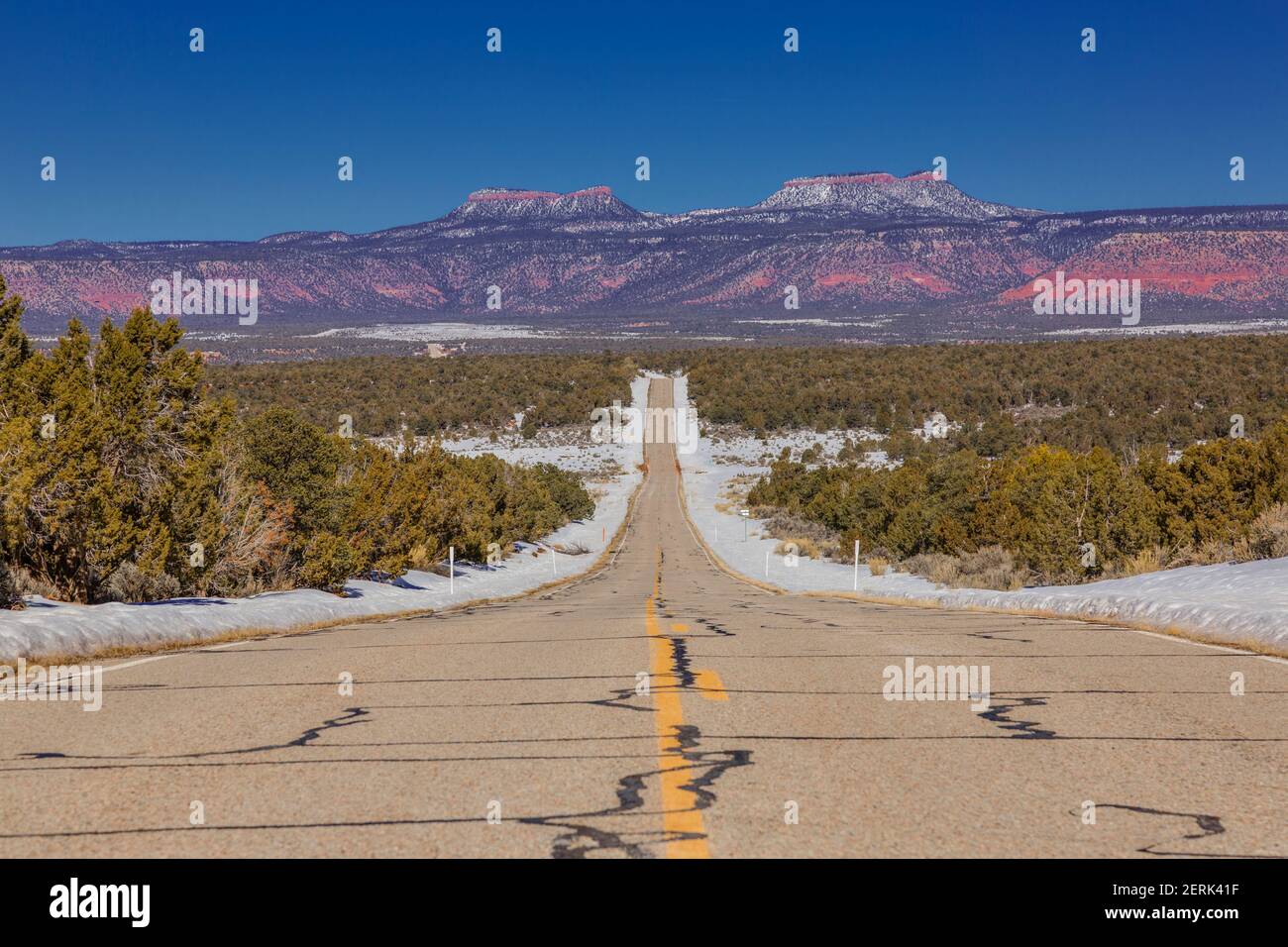 Vista panoramica lungo una strada vuota e infinita con orecchie di orso montagne sullo sfondo in inverno Foto Stock