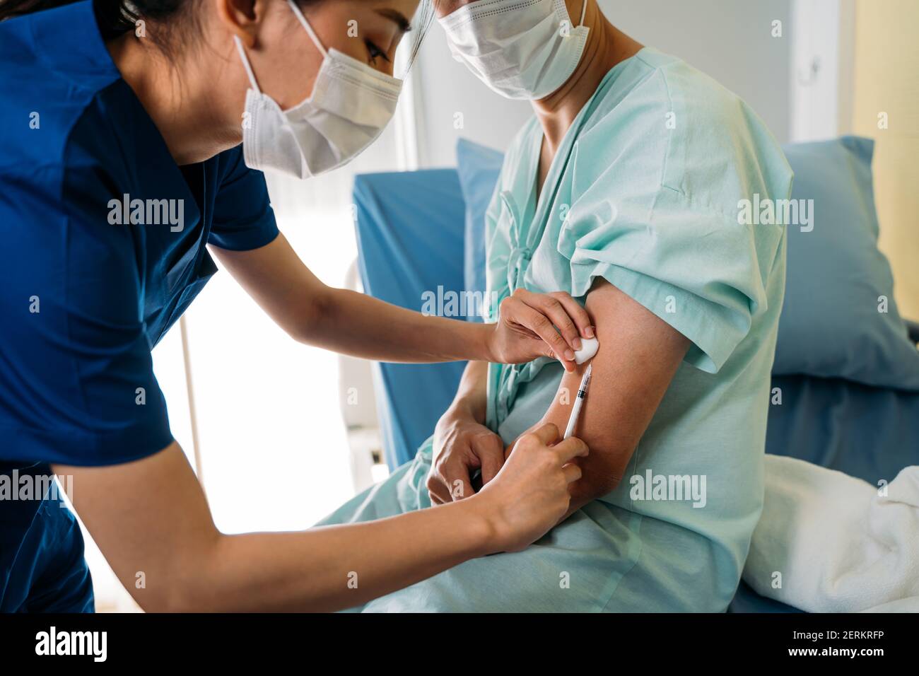 Primo piano di una giovane dottoressa in maschera uniforme durante l'iniezione di vaccinazione a un paziente giovane di sesso maschile che indossa un maschera per la sicurezza contro la pandemia di covid-19 Foto Stock