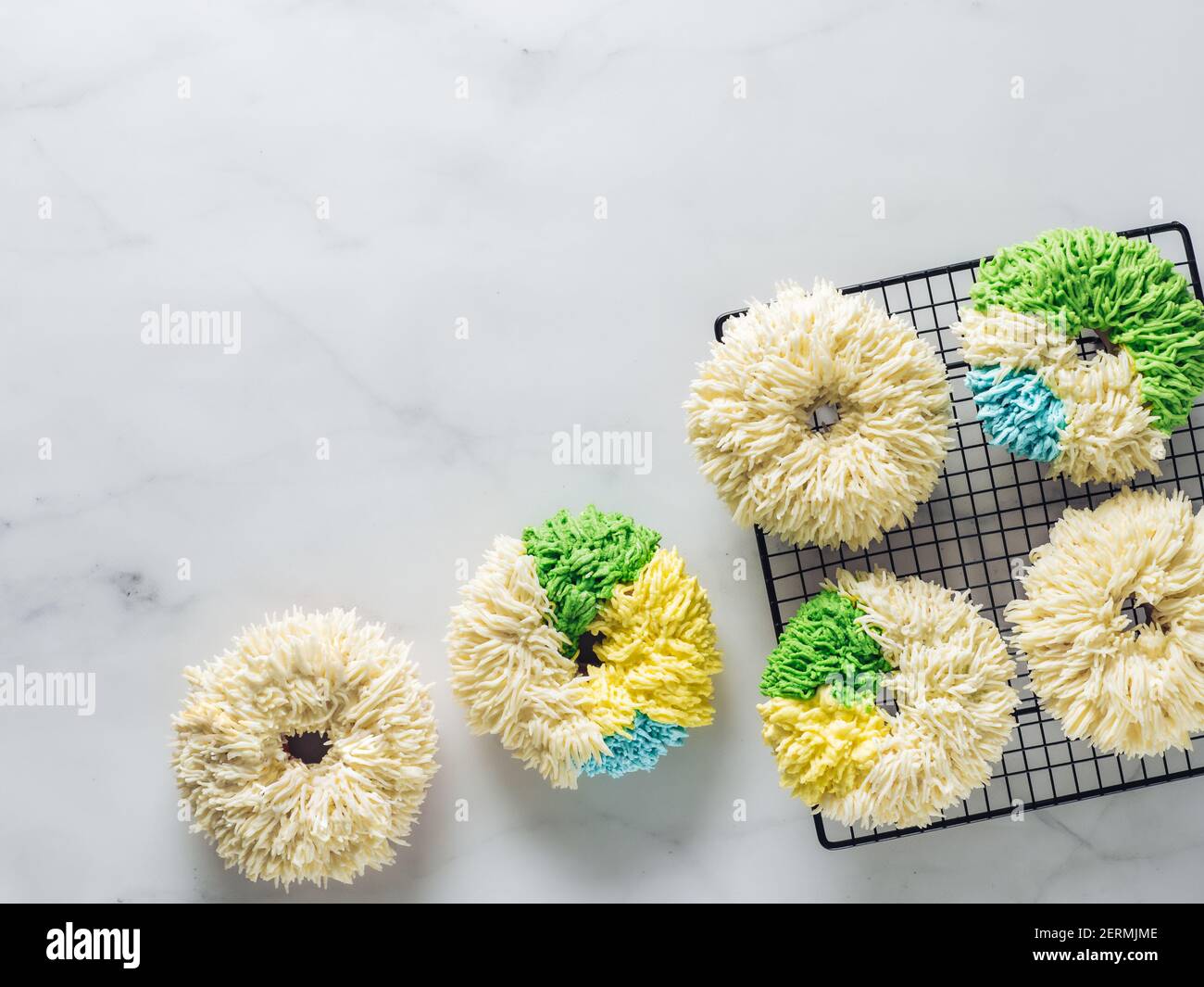 Ciambelle Shag su sfondo di marmo bianco. Inusuale ciambelle colorate alla moda con crema alla vaniglia. Spazio di copia. Vista dall'alto o piatta. Foto Stock