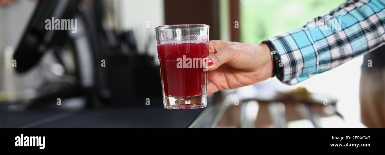 La mano della donna tiene il vetro nel caffè con liquido rosso simile alla frutta o alla gelatina Foto Stock