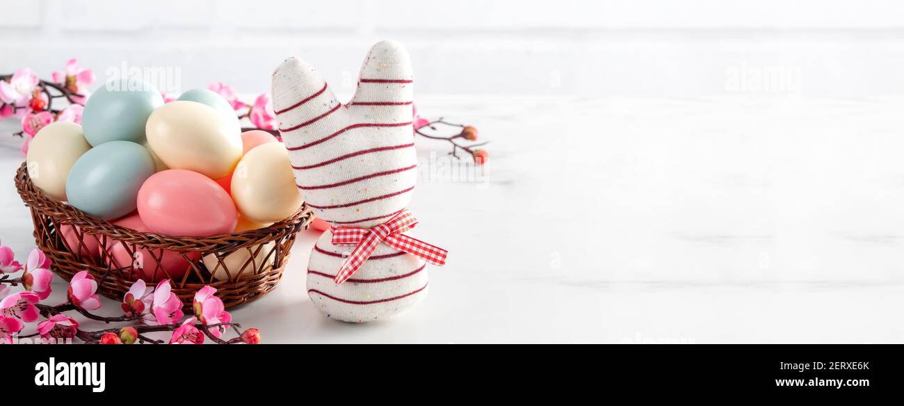 Primo piano di uova di Pasqua colorate nel nido con fiore di prugna rosa su sfondo di tavola di legno bianco luminoso. Foto Stock