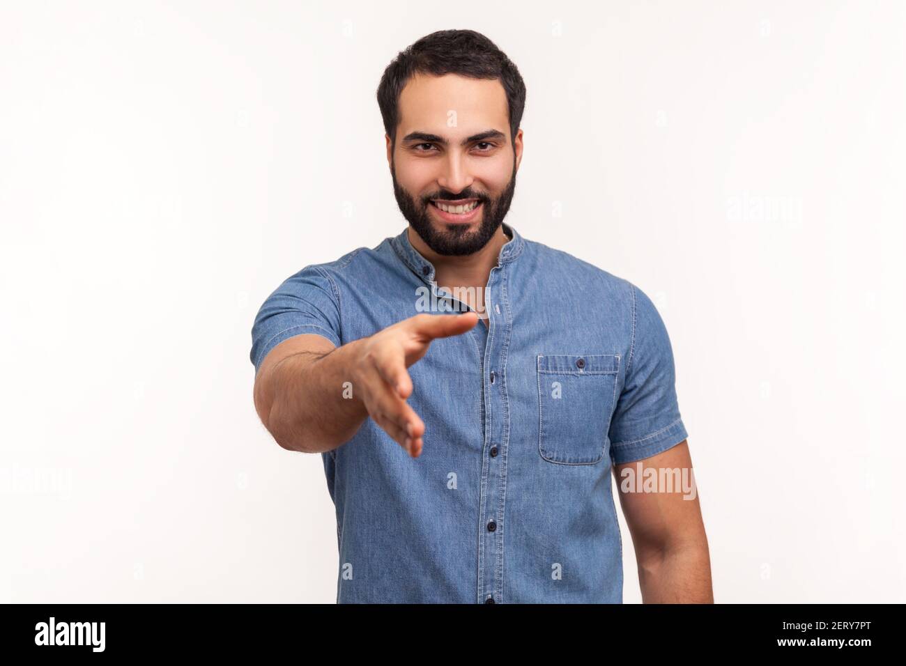 Uomo sorridente amichevole con barba in camicia blu tenendo la mano per la stretta di mano, felice di fare accordo, partnership di successo. Studio interno isolato Foto Stock