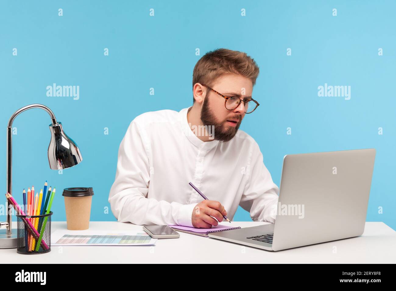 Serio lavoratore concentrato di lavoro di ufficio di uomo che prepara il discorso che cerca le informazioni sul laptop e che scrive giù al blocco note, facendo le note. Studio interno Sho Foto Stock