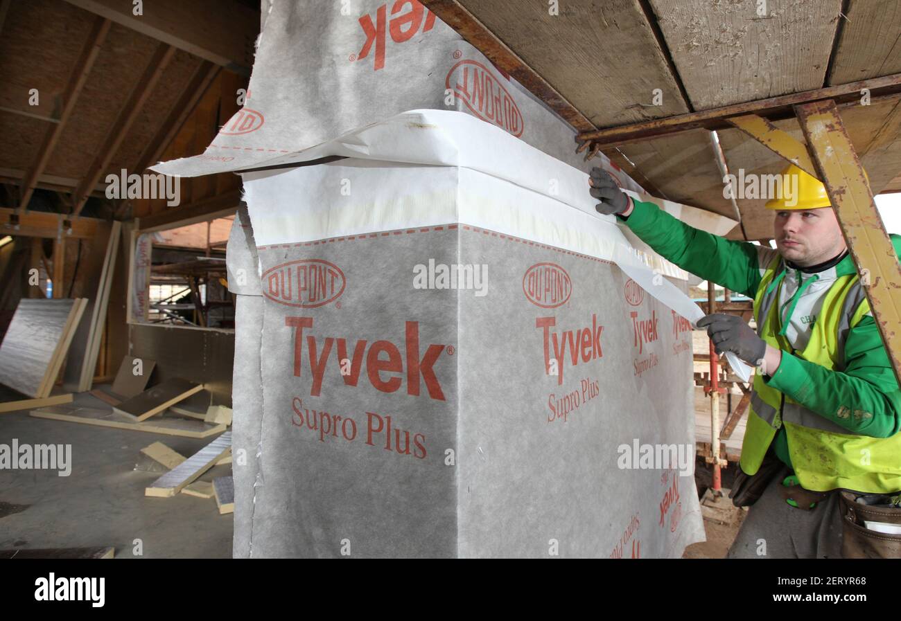Lavoratori edili che applicano la lastra Tyvek con barriera all'aria e all'acqua a. edificio parzialmente costruito Foto Stock