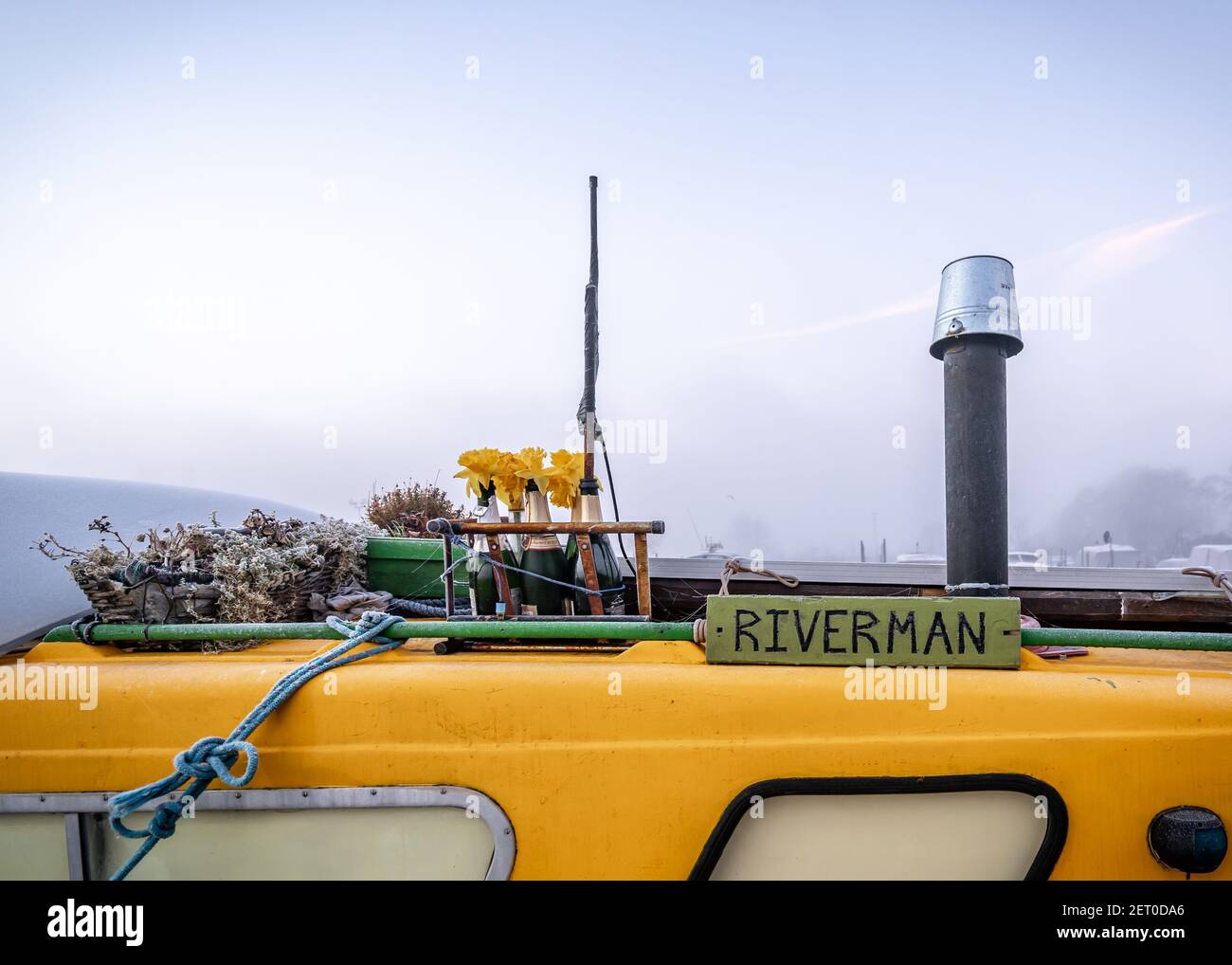 Riverman barca casa canale stretto decorata con bottiglie contenenti luminoso fiori di primavera giallo del daffodil e camino di metallo sul tetto della nave in alto Foto Stock