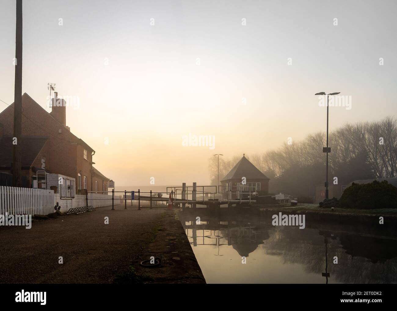Misty nebbia bella mattina tranquilla lungo il canale del fiume canale corso d'acqua. Nuvole dorate e nocciole. Riflessi in acqua vecchia industria serena calma lungofiume. Foto Stock