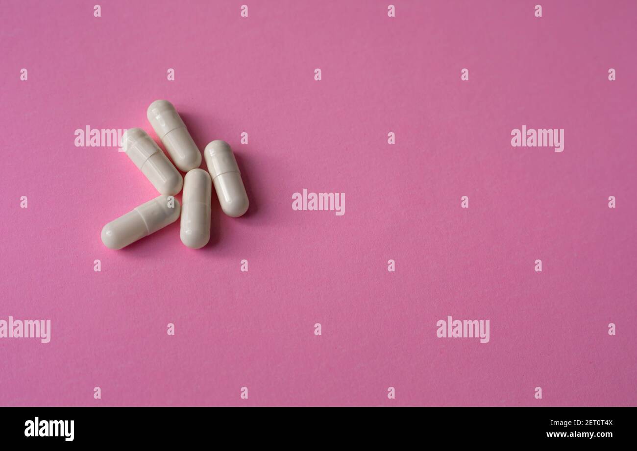 Capsule, pillole o compresse di grandi dimensioni bianche su sfondo rosa Foto Stock