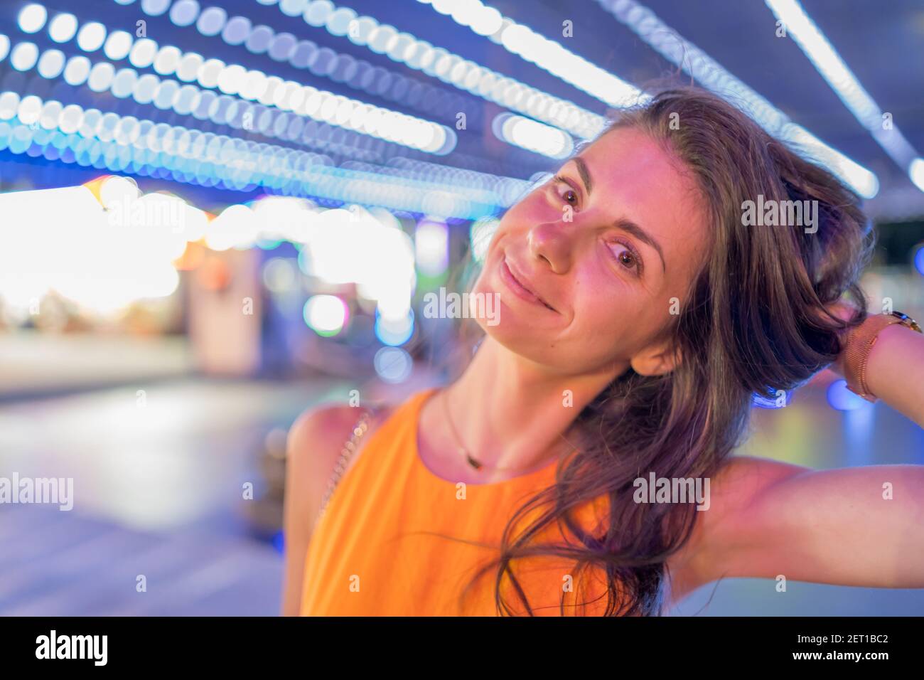 Ritratto di donna bruna sorridente in abito arancione, tenendo i capelli con una mano. Foto Stock