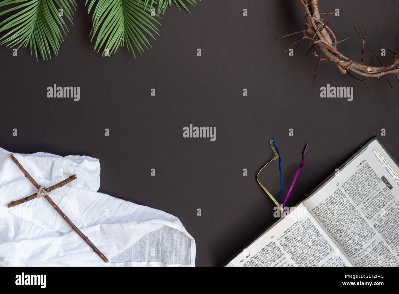 Cornice di bibbia aperta, corona di spine, foglie di palma e croce cristiana su sfondo nero con spazio copia Foto Stock