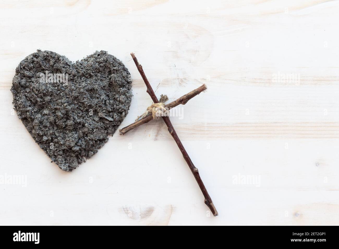 Semplice croce cristiana in legno e un cuore di ceneri su sfondo bianco in legno con spazio copia Foto Stock