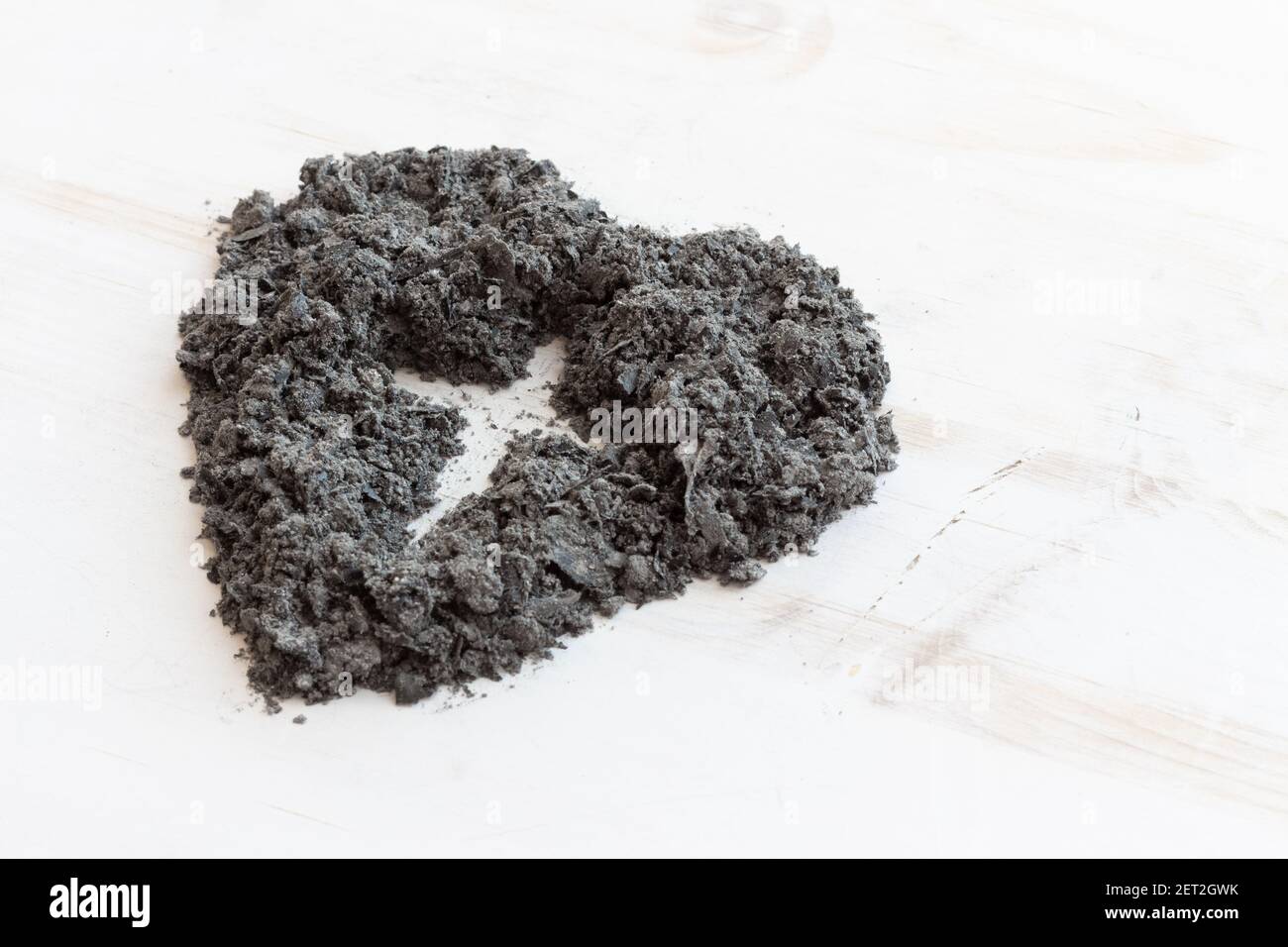 forma di una croce cristiana in un cuore di cenere su sfondo di legno bianco con spazio copia Foto Stock