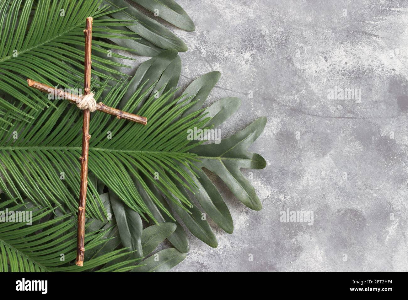 Croce di legno su sfondo grigio con foglie di palma e grigio sfondo Foto Stock