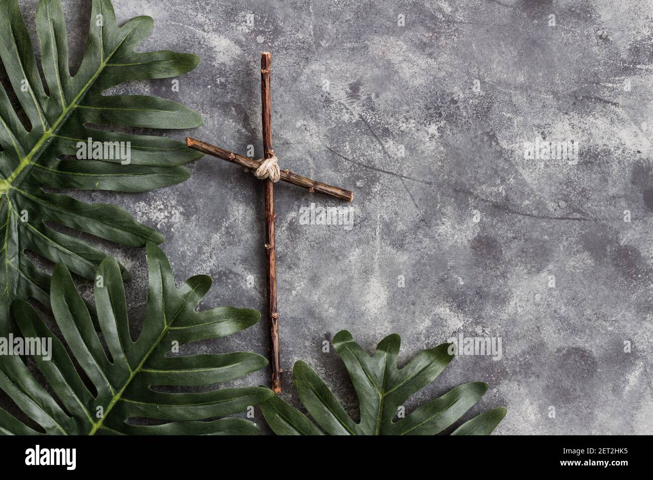 Foglie di palma e croce di legno su sfondo grigio Foto Stock