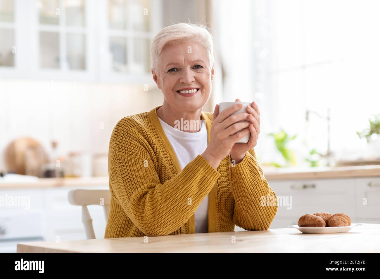 Signora anziana allegra che beve caffè con croissant Foto Stock