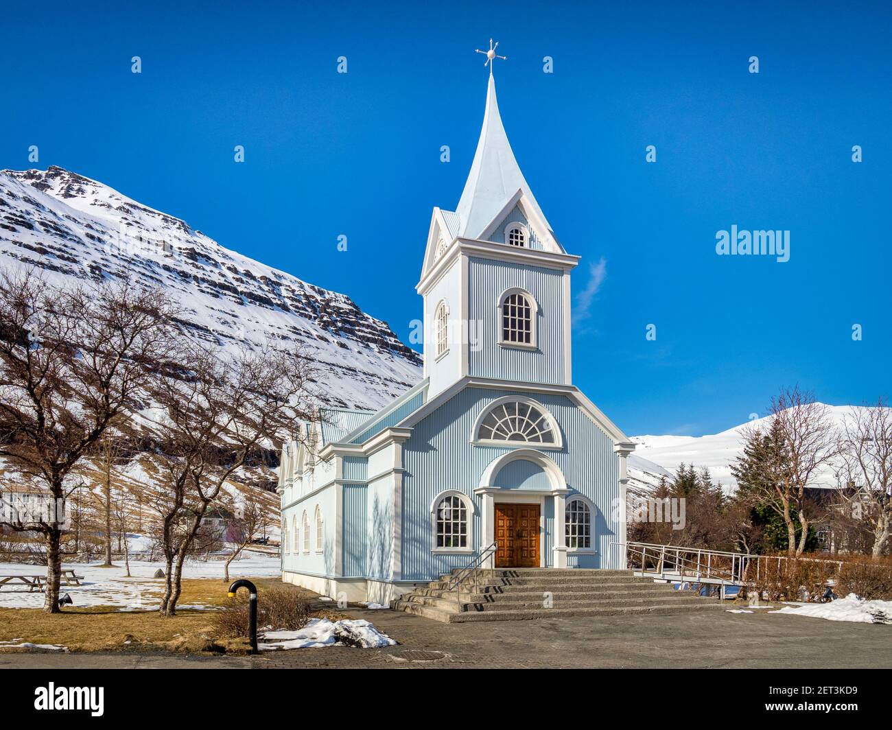 La famosa chiesa blu a Seyðisfjörður Affitto, Est Islanda, su una luminosa giornata di primavera con montagne innevate. Foto Stock