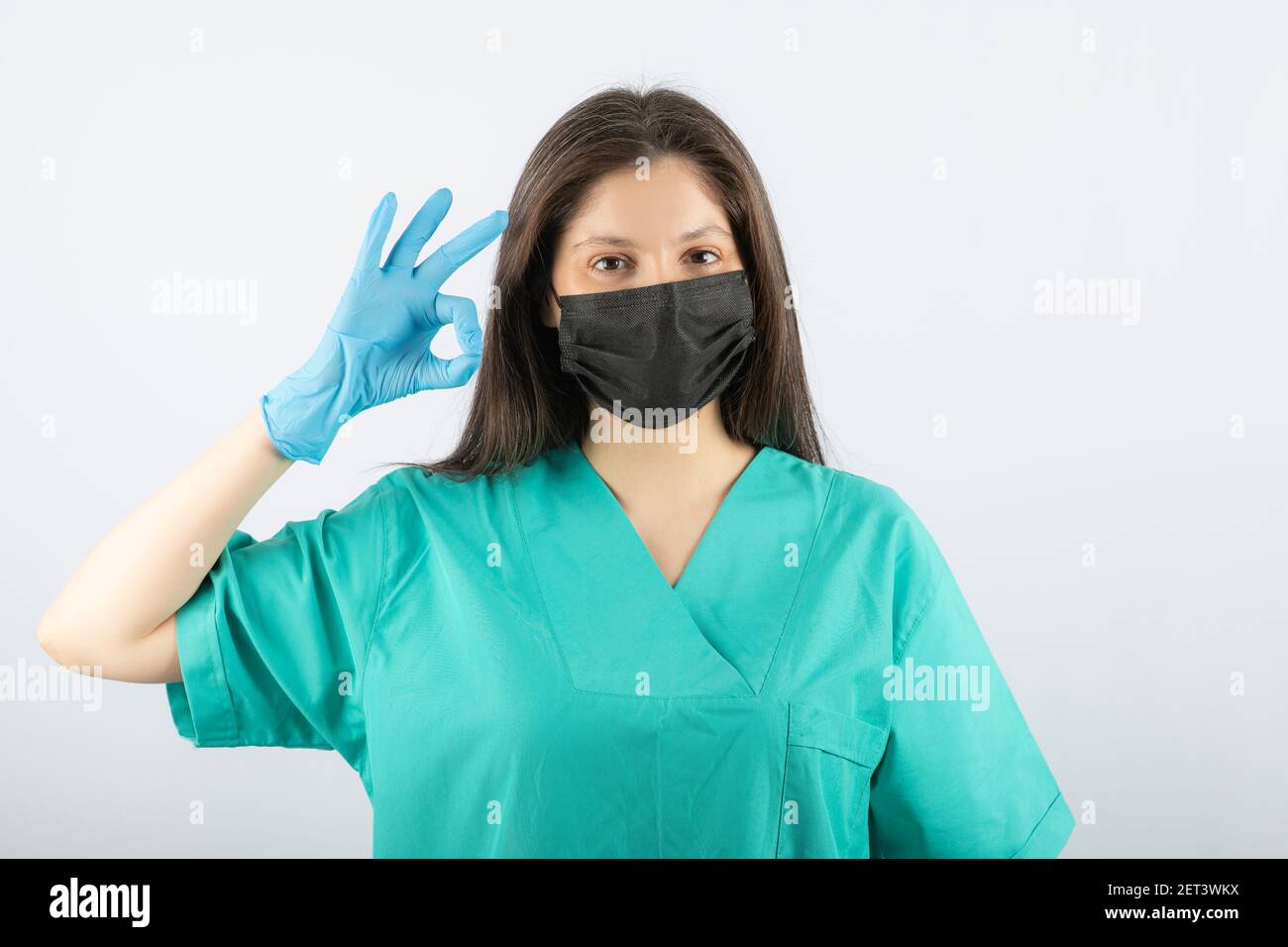 Donna medico indossando maschera medica nera e mostrando un gesto ok Foto Stock