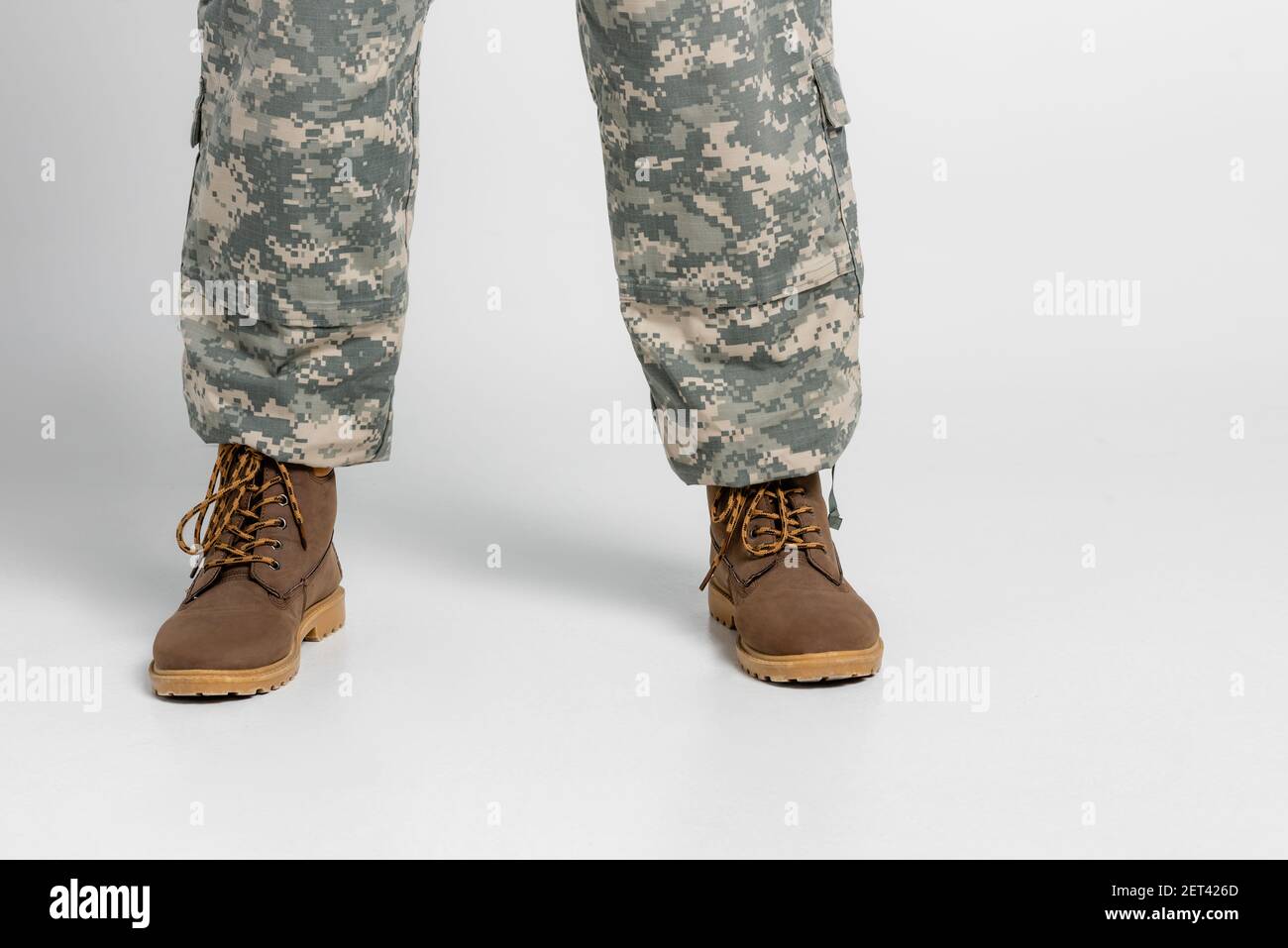 Vista ritagliata del soldato con pantaloni e stivali militari sfondo grigio Foto Stock