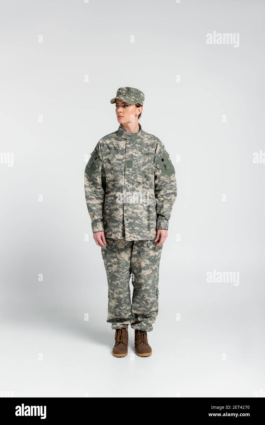 Donna in abiti militari in piedi su sfondo grigio Foto Stock