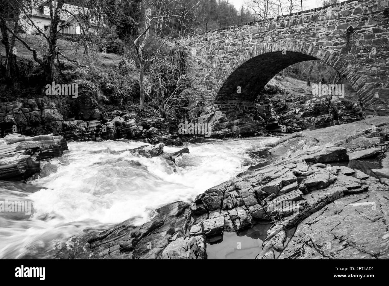 Un singolo ponte di pietra ad arco che attraversa la Feshie che scorre veloce Fiume nel Cairngorm National Park nelle Highlands scozzesi in bianco e nero Foto Stock
