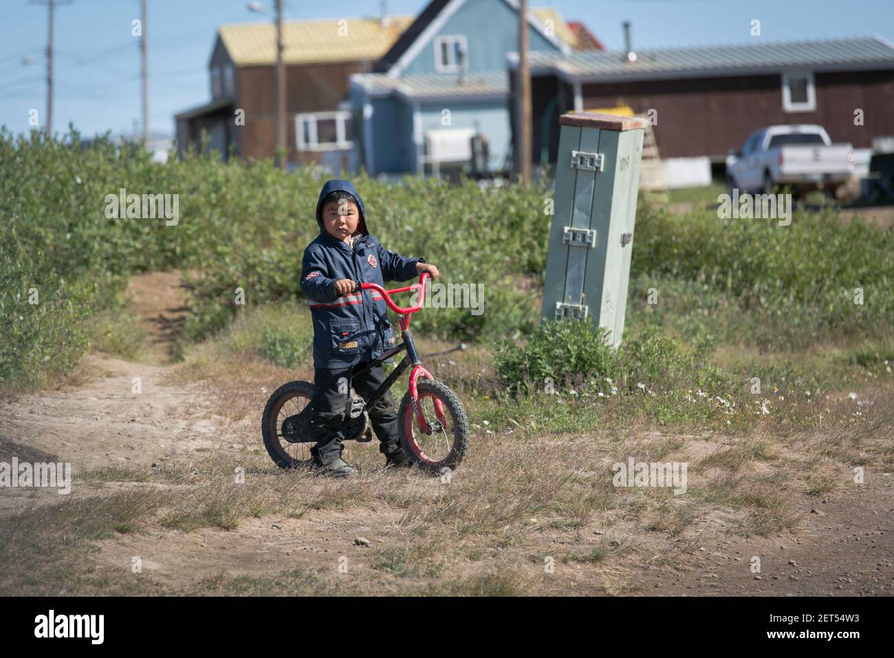 Bambino giovane indigeno con la sua bicicletta in estate, nel villaggio Inuvialuit di Tuktoyaktuk, territori del Nord-Ovest, Artico del Canada. Foto Stock