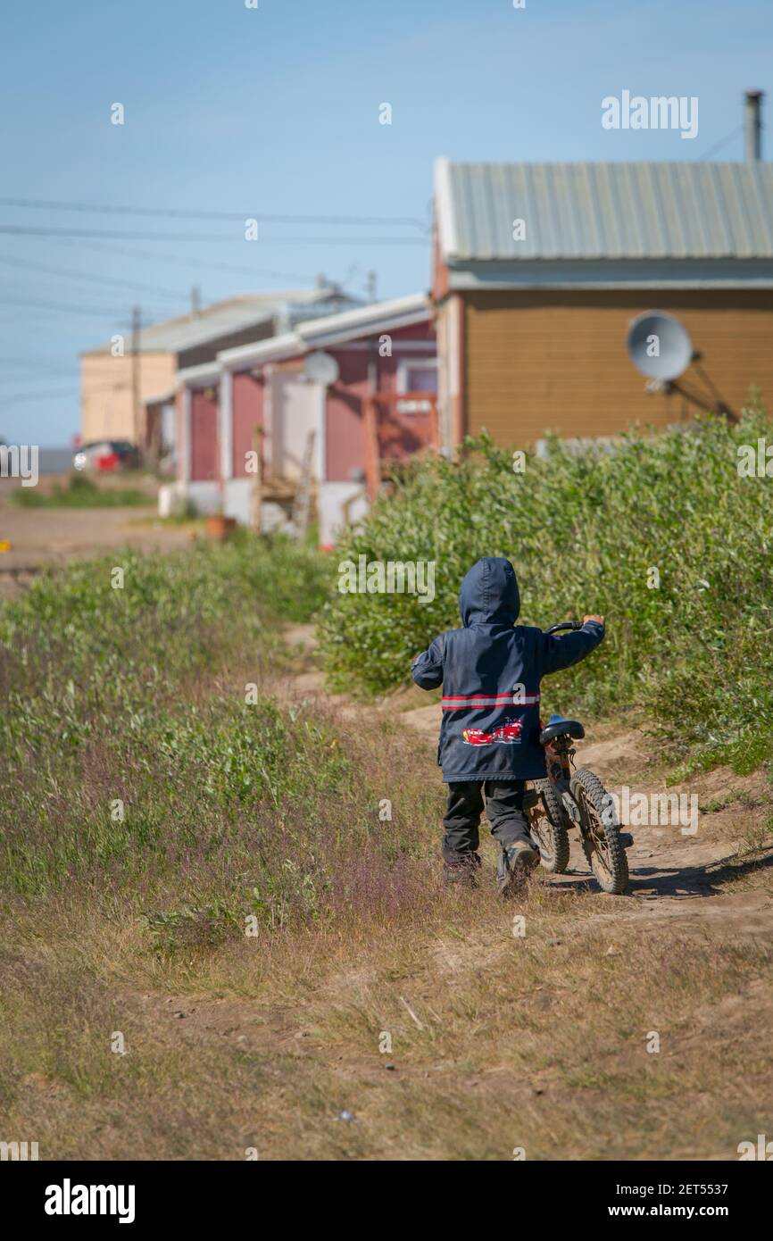 Bambino giovane che cammina via con la sua bicicletta in estate nel villaggio Inuvialuit di Tuktoyaktuk, territori del Nord-Ovest, Artico del Canada. Foto Stock