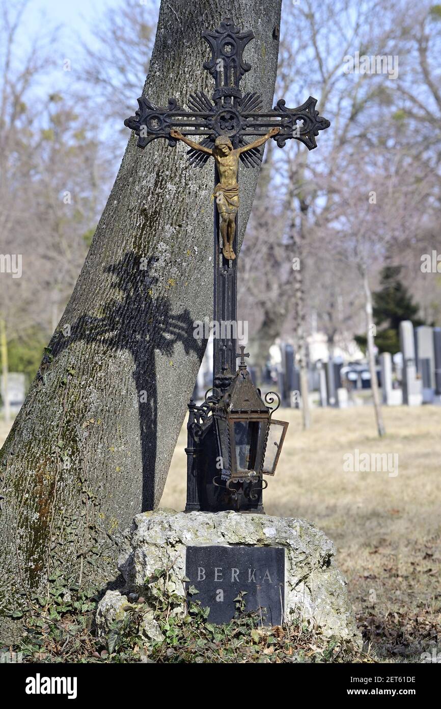 Vienna, Austria. Il cimitero centrale di Vienna. La vecchia croce di metallo getta ombre su un albero. Foto Stock