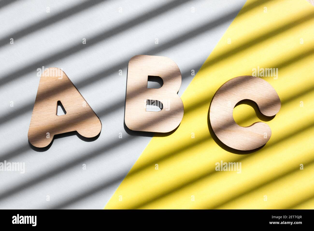 Lettere in legno ABC su sfondo blu e giallo. Il concetto dell'importanza dell'istruzione. Sfondo con ombre diagonali. Foto Stock