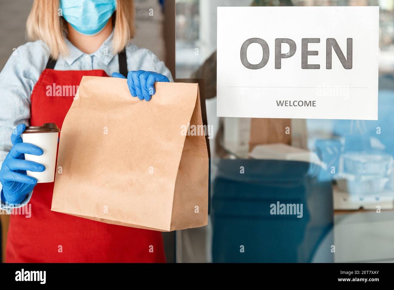 Riapertura del cartello della porta apertura di benvenuto dopo la chiusura a chiave sull'ingresso della porta d'ingresso. Riaprire la nuova normale. Cameriera donna in maschera medica protettiva e guanti gi Foto Stock