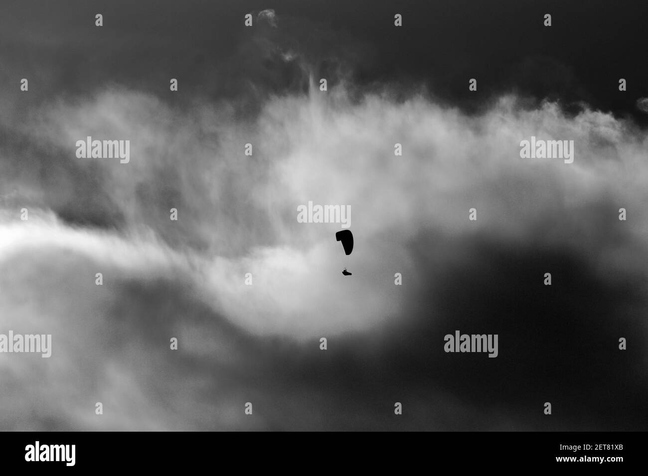 Artistico, contro la foto chiara, in bianco e nero, della sagoma di un parapendio solo in mezzo alle nuvole. Foto Stock