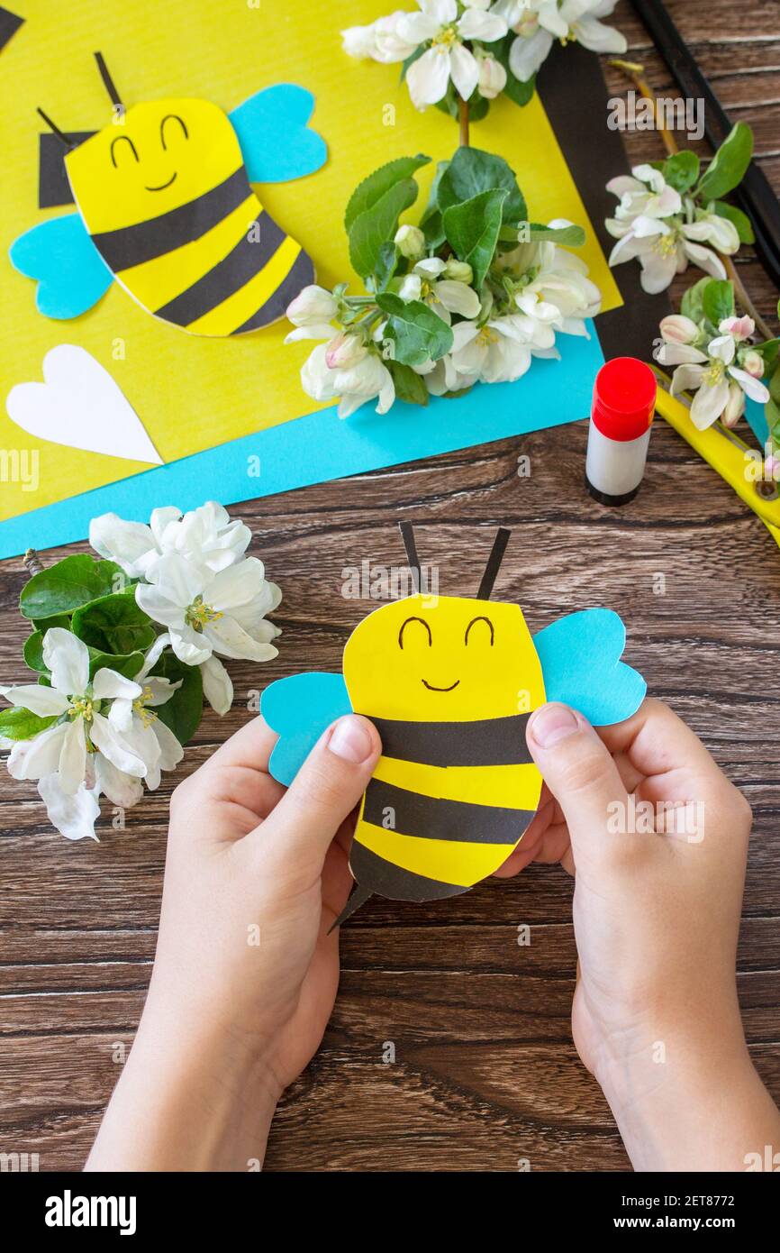 Bambino che tiene il giorno della mamma biglietto d'auguri - ape con primavera fiori di mela albero. Progetto di creatività per bambini, fatti a mano, artigianato per bambini. Foto Stock