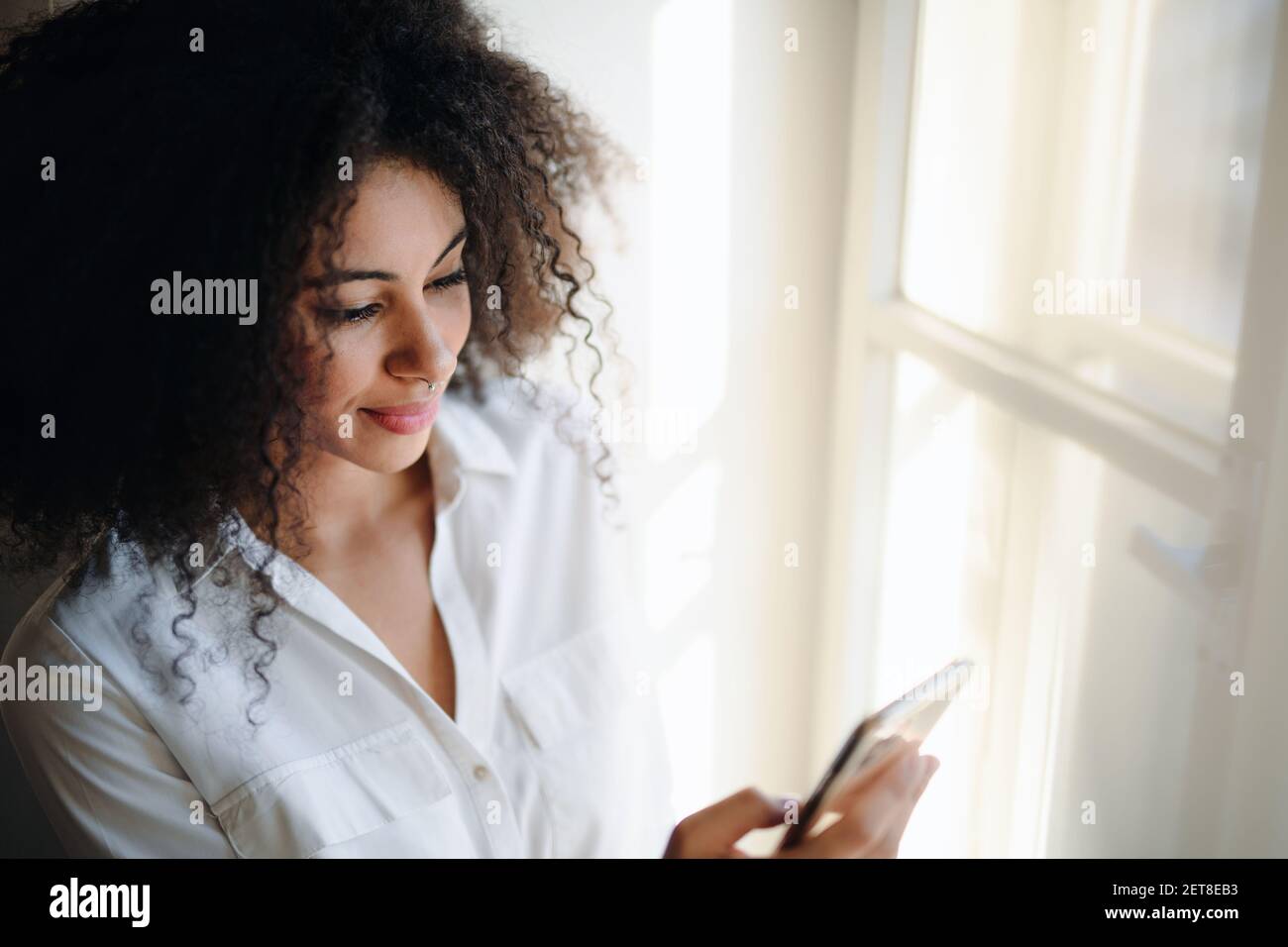 Ritratto di giovane donna sul davanzale della finestra all'interno di casa, utilizzando lo smartphone. Foto Stock