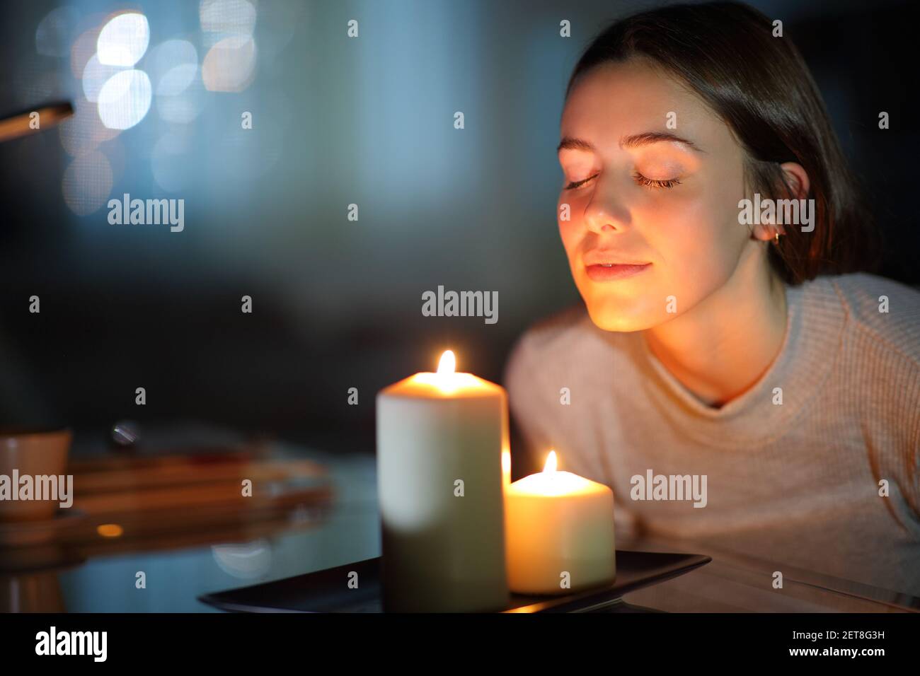 Donna rilassata che annusa una candela illuminata profumata di notte a casa Foto Stock