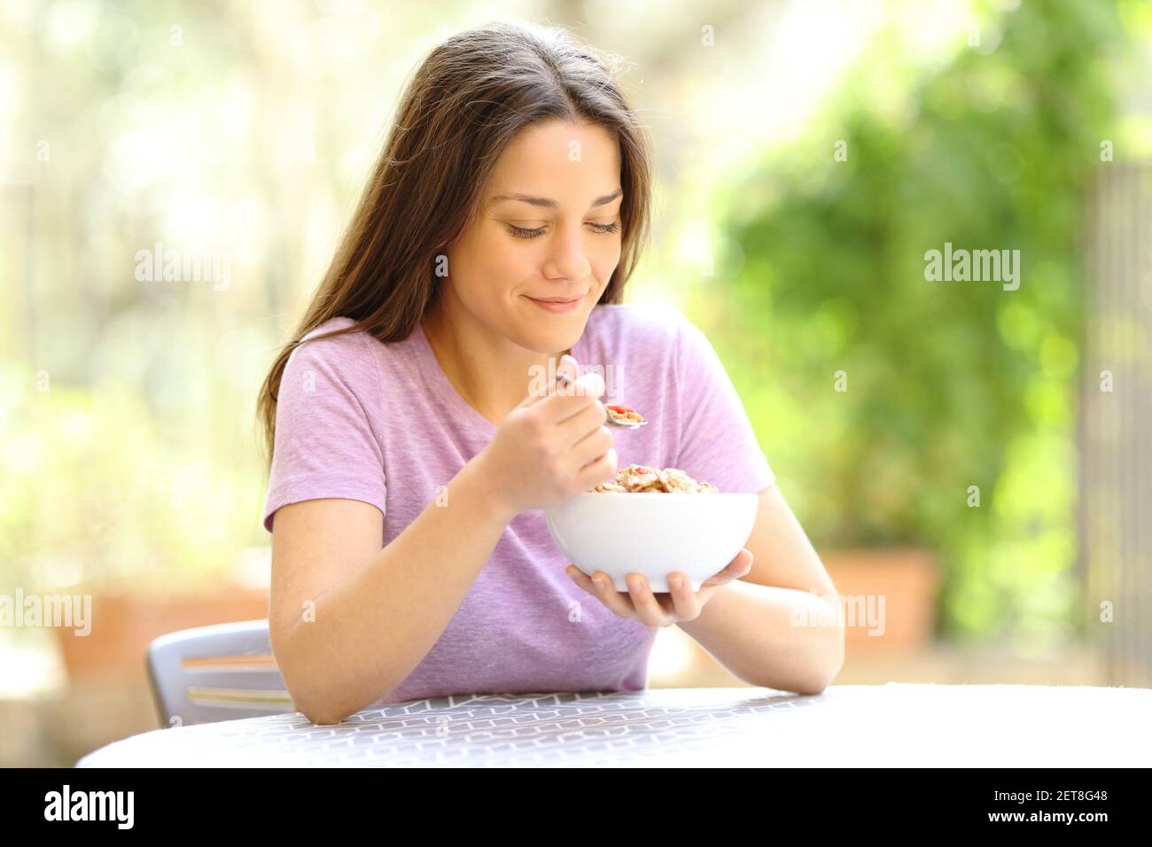 Donna felice che mangia cereali al mattino seduto in un giardino a casa Foto Stock