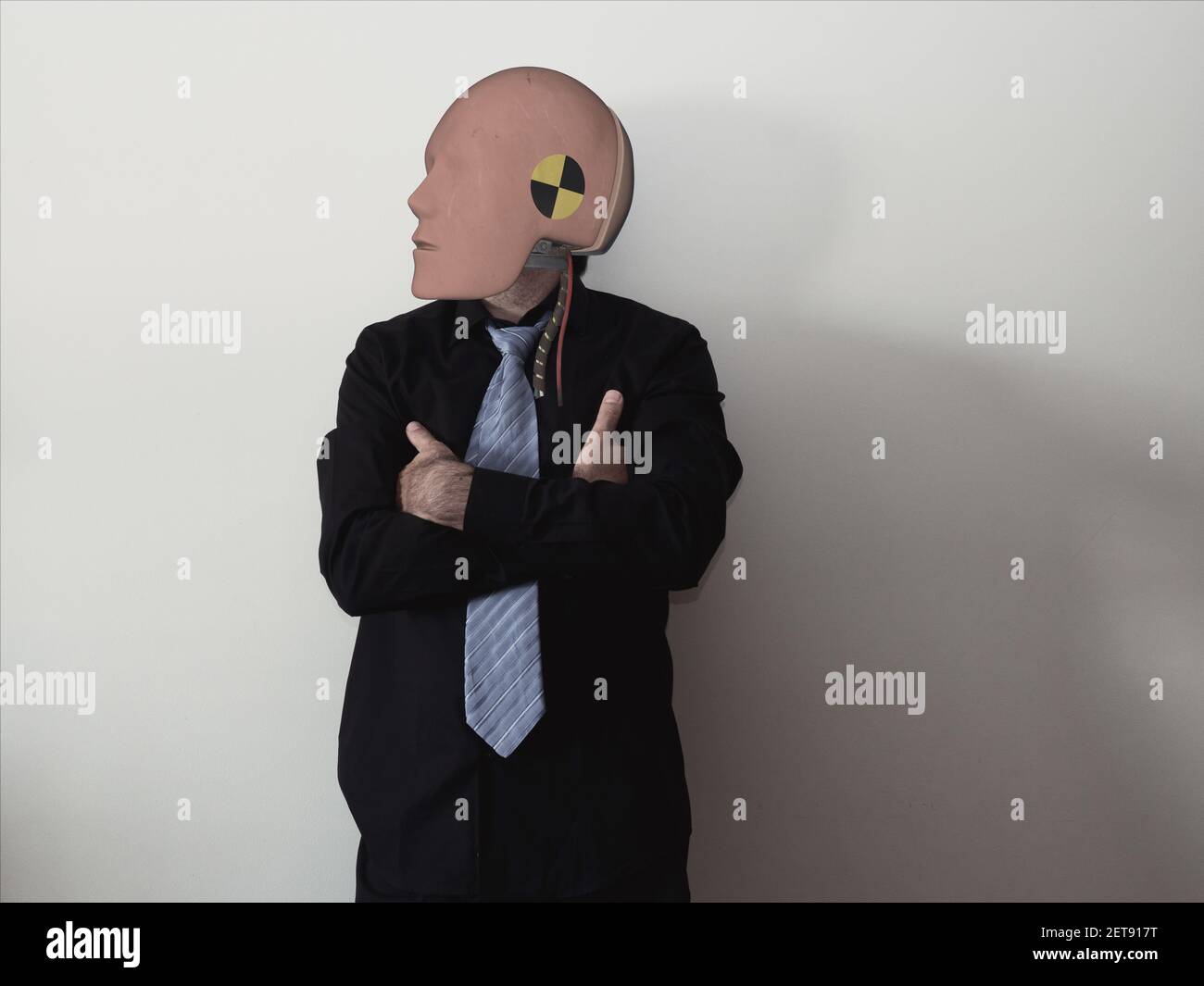 Un uomo con una testa resa irrealistica che indossa una cravatta e in piedi con mani incrociate Foto Stock