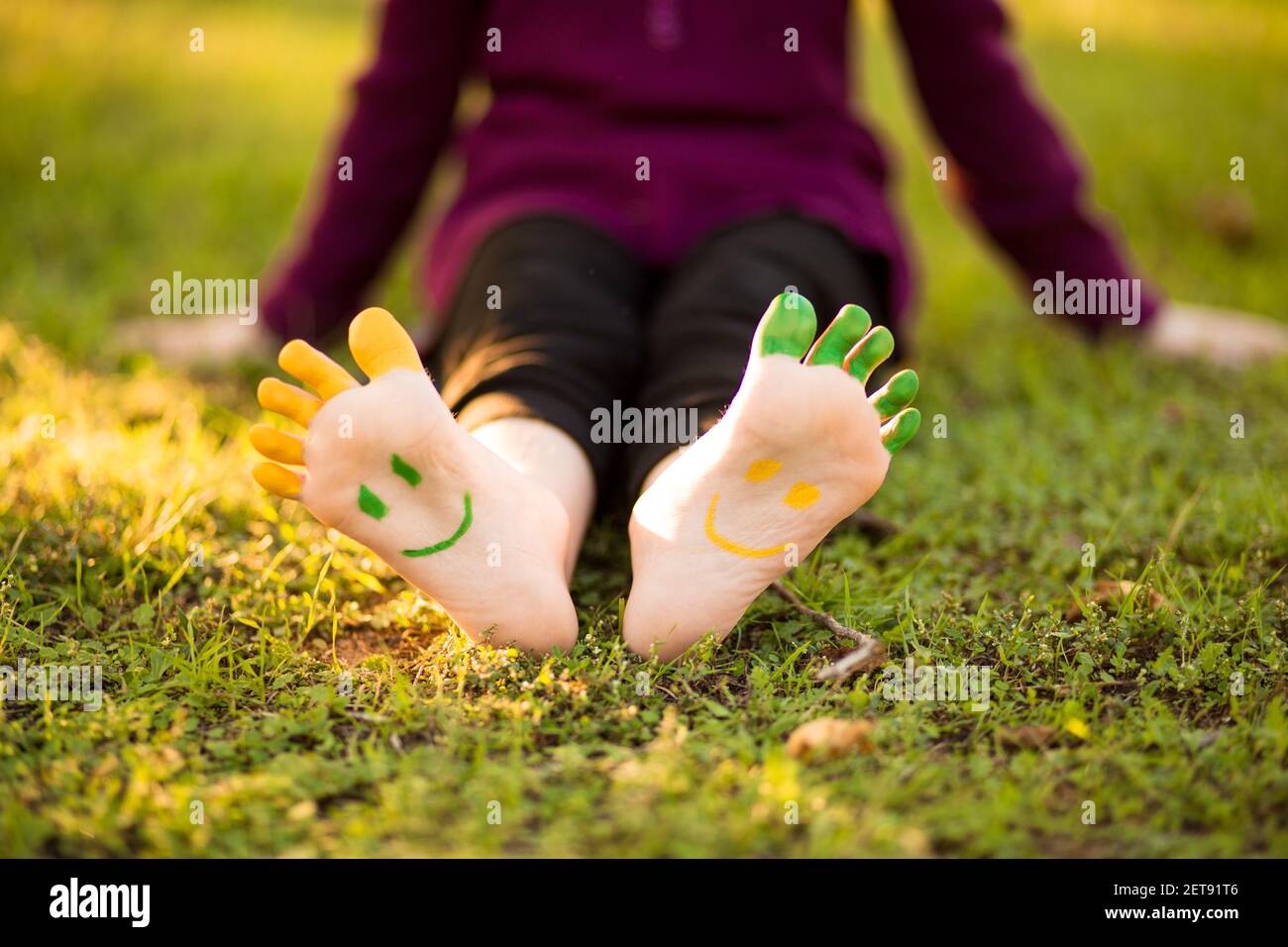 Bambina con piede dipinto su erba verde divertirsi all'aperto nel parco primaverile. Foto Stock