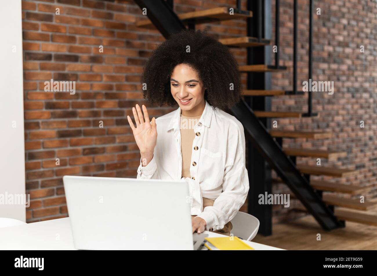 Afroamericana attraente donna al laptop che chattano via video a casa, felicemente salutato con un amico, relazione a lunga distanza, auto-isolamento durante la quarantena, nuova realtà, riunione virtuale Foto Stock