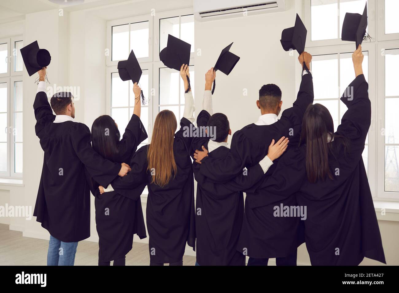 I laureati alzano le mani dalle tavole di Malta accademiche mentre si levano in piedi in classe. Foto Stock