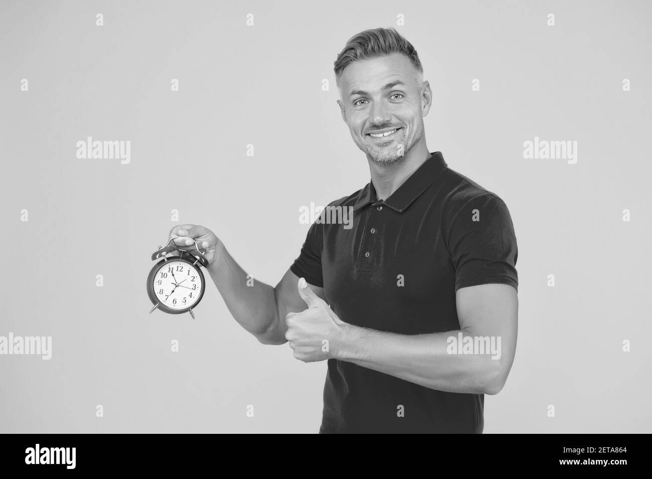 Precisione e precisione. Happy man tiene sveglia mostrando pollici in su. Puntualità e puntualità. Precisione raggiunta. Tempo standard. Foto Stock