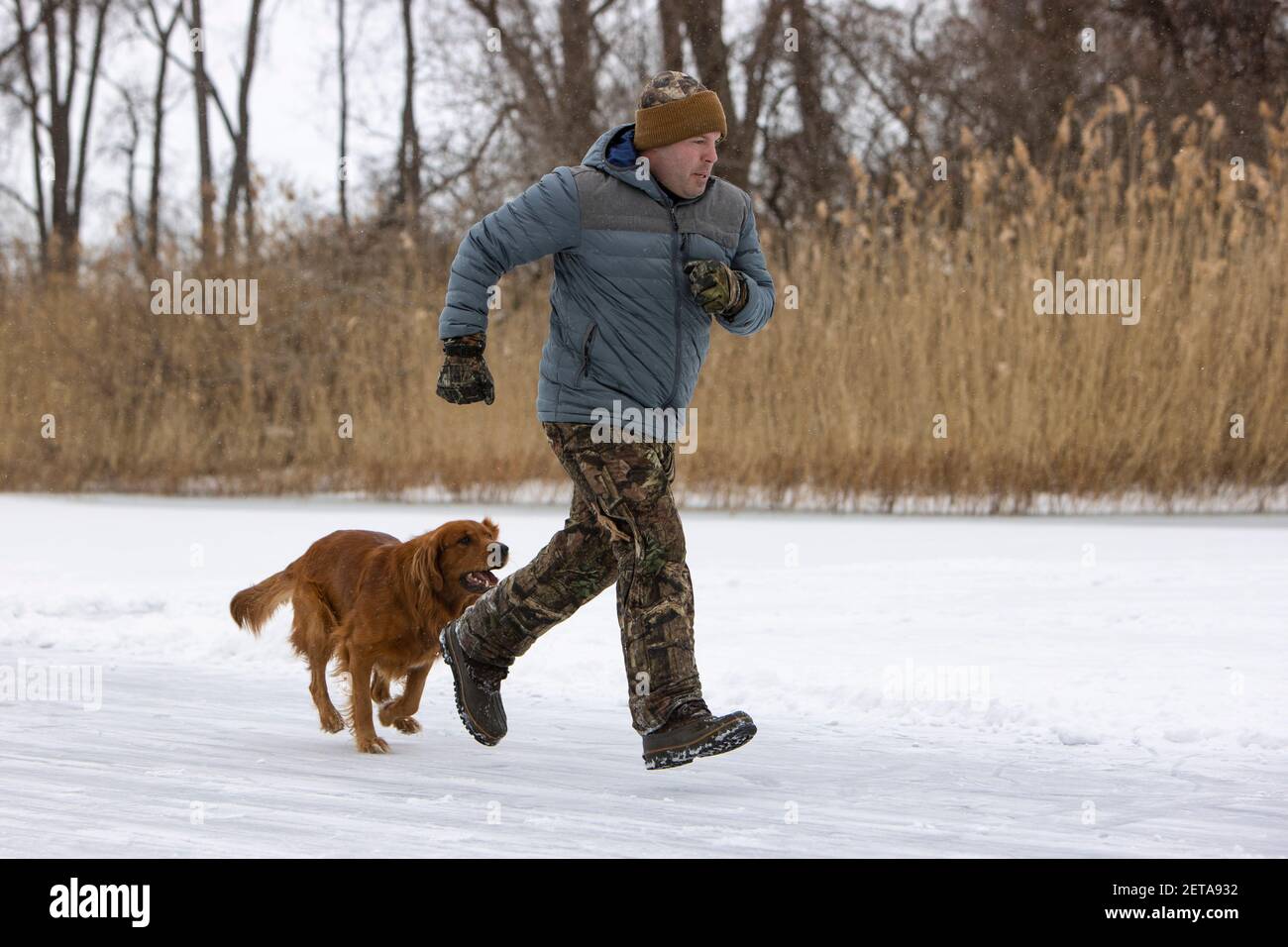 L'uomo e il suo cane che corrono insieme su un laghetto ghiacciato. Foto Stock
