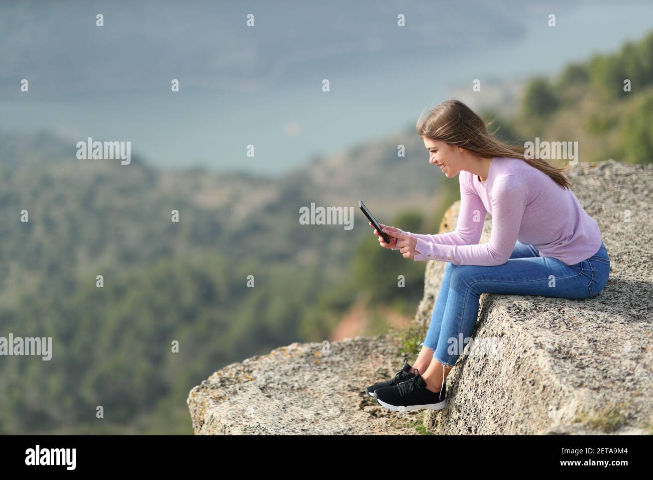 Il ritratto di vista laterale del bofy completo di un controllo teen felice smartphone in una scogliera Foto Stock