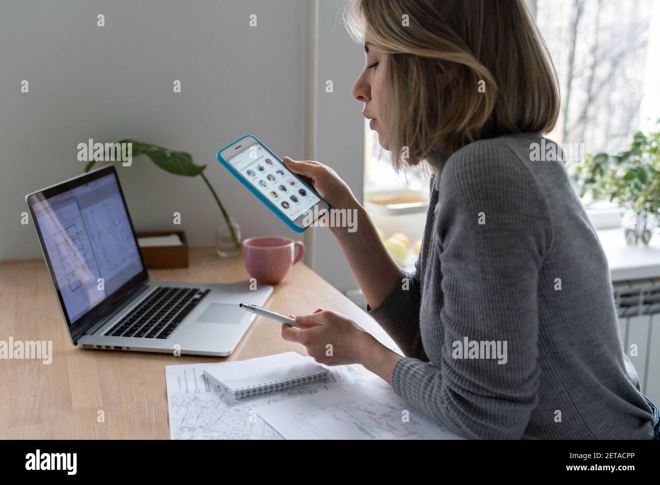 Donna designer che utilizza smartphone, prende una pausa dal lavoro e ascolta la voce in clubhouse Foto Stock