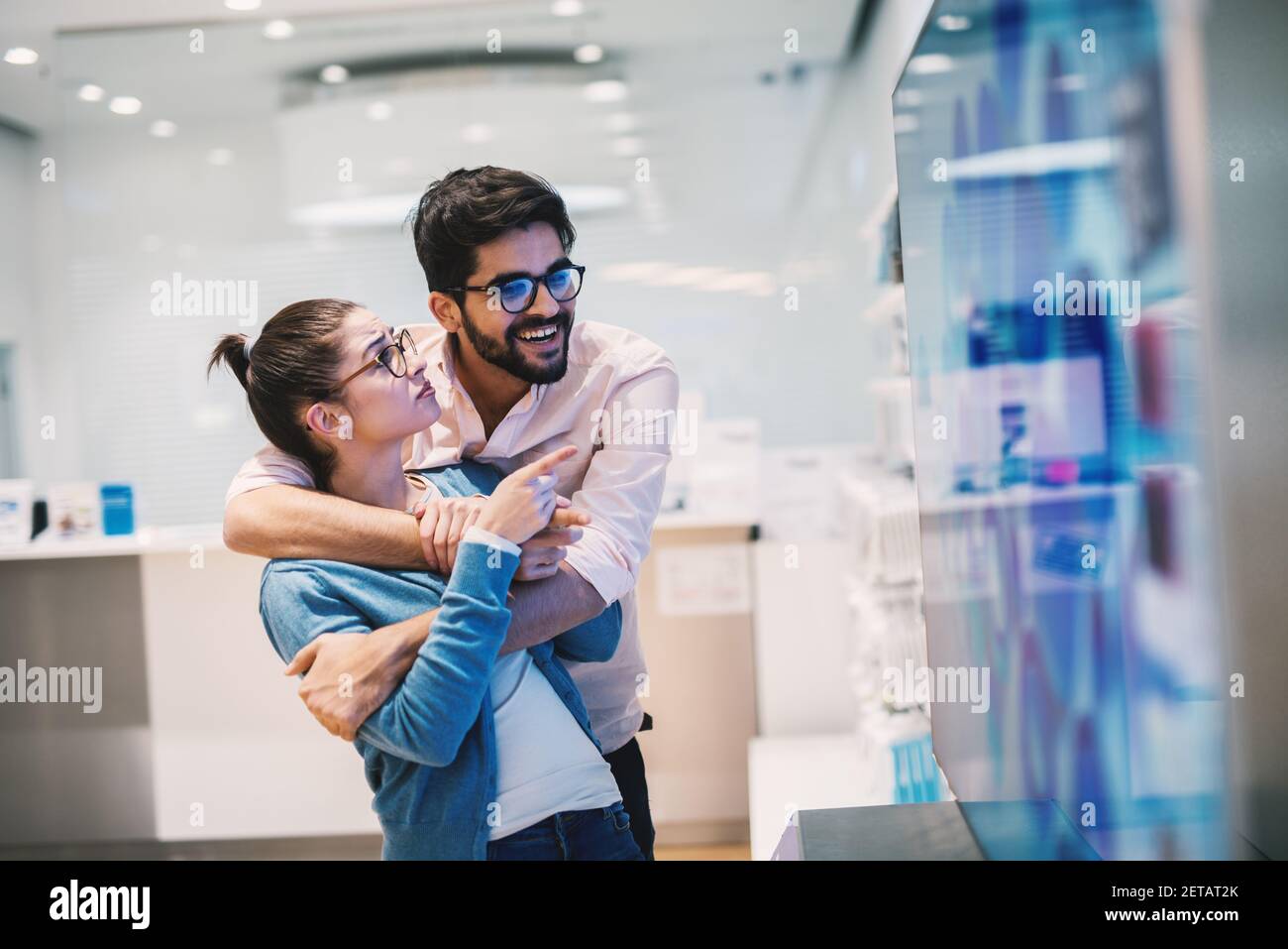 Giovane bell'uomo allegro sta tenendo la sua fidanzata abbracciata come sta navigando telefoni in un negozio luminoso. Foto Stock