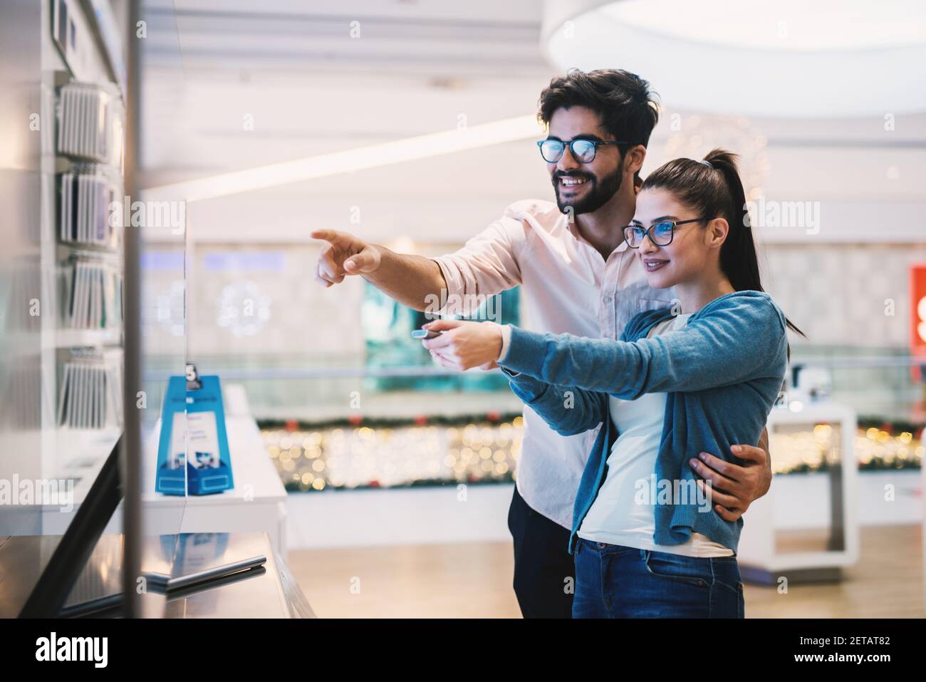 Giovane bella coppia allegra sta testando un grande flat TV in un negozio di hardware tecnologico. Foto Stock